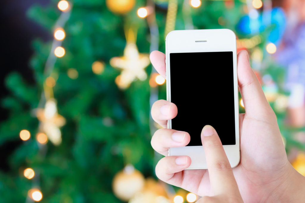 Christmas party concept - hand holding mobile smart phone with Christmas lights bokeh on Xmas tree